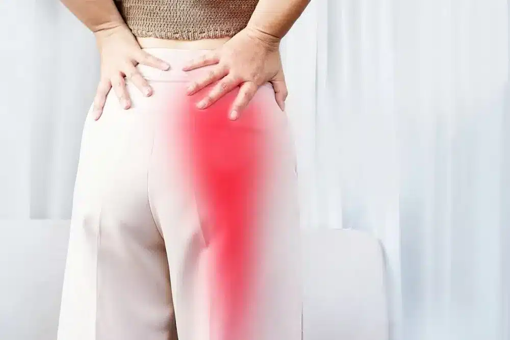 Sciatica pain radiating from the lower back down the leg. Person holding their lower back with red highlighted pain running down the leg, indicating sciatica.